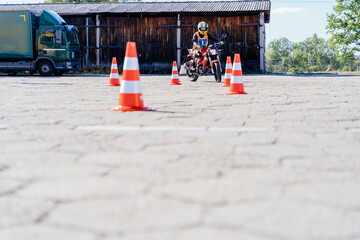 L-driver person drives slalom through the orange cones on motordrome on motorcycle