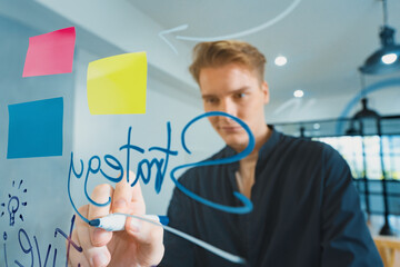 Professional caucasian businessman brainstorming marketing idea by using mind map and sticky notes on glass board at modern meeting room. Creative business and planing concept. Immaculate.