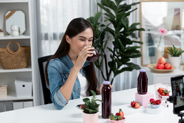 Smiling young beautiful Asian reviewing tasty mixed strawberry and cherry juice detox drinks,...