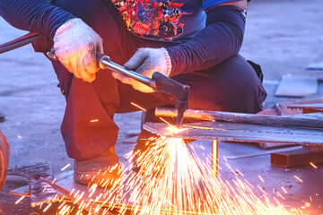 Cropped image of welder is cutting iron plate with acetylene gas welding torch machine for ship improvement work at shipyard in the evening