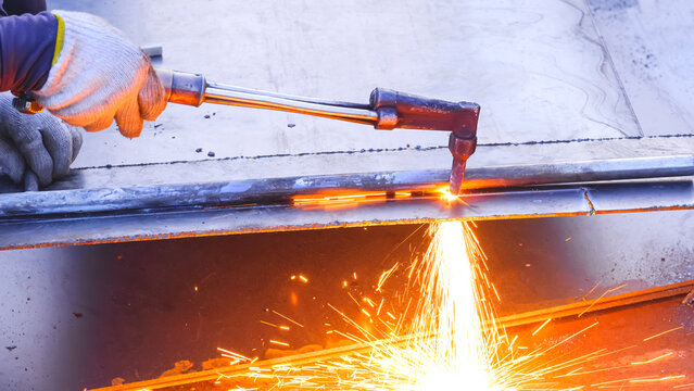 Close up of welder hand is cutting black steel plate with acetylene gas welding torch machine at outdoor workshop