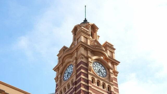 Melbourne's iconic Flinders Street Railway Station clock tower stands majestically against a beautiful blue sky, captured in a close-up shot.