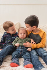 Toddler brothers comforting crying baby brother while sitting on bed