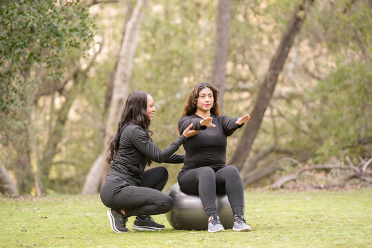 Women trainer showing a person on a workout ball in the woods