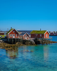 Reine, Lofoten, Norway,A group of traditional red houses with grass roofs stand on stilts in the crystal clear water of a Norwegian fjord.