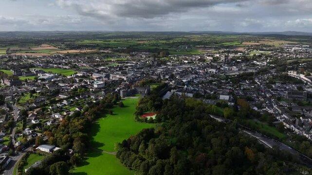 Kilkenny Castle, County Kilkenny, Ireland, September 2023. Drone at a higher angle orbits the estate with views north west towards St Canice's Cathedral and Saint Mary's Cathedral in the distance.
