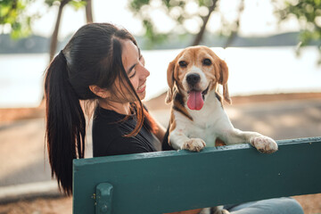 Asian woman resting with beagle dog on bench after walk in park