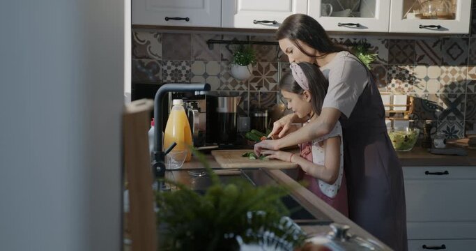 Young woman teaching child helpful daughter to make salad from fresh vegetables cooking healthy meal in kitchen at home. Family and nutrition concept.
