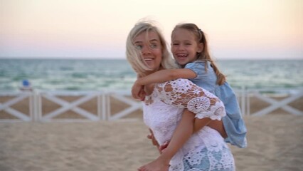 Happy family funny plays and walks along beach in summer evening by sea at sunset. Mother carries daughter on back. Travel, vacation, holiday - Powered by Adobe