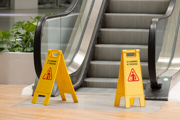Two yellow caution signs are placed on the steps of an escalator