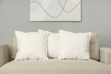 Soft white pillows on sofa near grey wall indoors