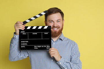 Making movie. Smiling man with clapperboard on yellow background