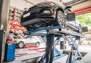 mecanico trabajando bajo automovil sobre plataforma elevador en taller 