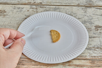 Hand holding a fork over a plate with one half of a cracker, last bite of food, lack of food, rigid diet, small portion of food