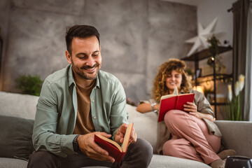 Boyfriend and girlfriend sit on sofa read book and discuss about that