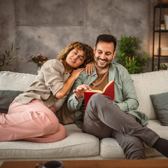 Boyfriend read a book while his girlfriend hug him at home