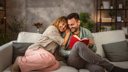 Obraz premium Boyfriend read a book while his girlfriend hug him at home