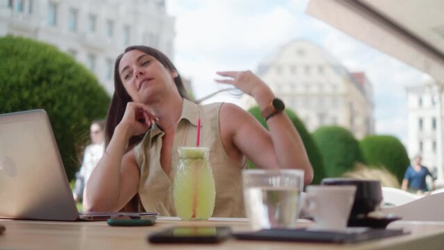 Smiling business woman using laptop sitting in outdoor cafe in downtown district
