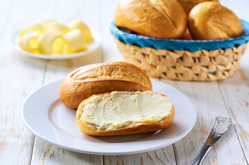 Basket of bread with butter on white wooden table.