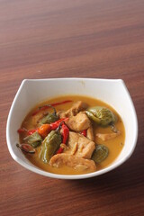 Ase cabe. Indonesian traditional food made of green chili and tofu cooked in rich coconut milk sauce. Served in white bowl on wooden table. Selective focus
