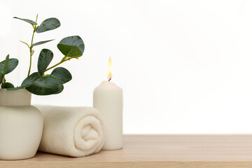 White candle, white towel, white vase with eucalyptus leaves.