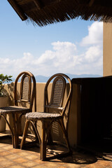 Two wicker chairs under a thatched roof on a sunny patio outdoor with a clear sky and mountain view in the afternoon mediterranean bar