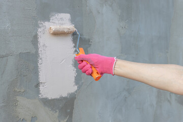 A person is painting a wall with a roller and wearing pink gloves