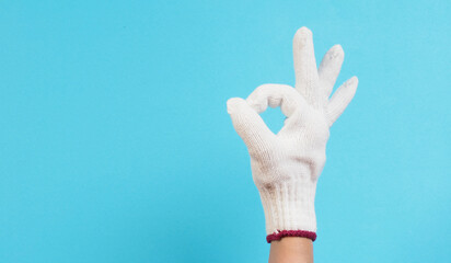 Hand is do OK hand sign and wear glove knitting on blue background.