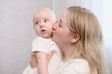 Woman mom gently kisses her newborn baby on cheek while holding him in her arms, showing heartfelt gesture of love and tenderness. Concept of motherhood, maternity leave, infancy
