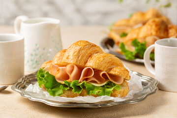 Chicken ham, cheese and lattuga croissant, breakfast table with coffee cups. Modern sandwich concept.