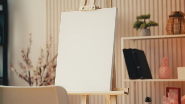 Wooden easel with a clean canvas standing in art studio, painting equipment