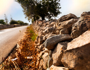 characteristic dry-stone wall of the Sicilian countryside flanks an asphalt road, fading into the horizon at sunset