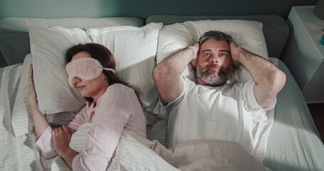 Mirthful man waking up at the bed and looking at his woman laying nearby. Man closed his ears...
