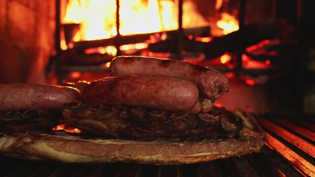 piled up meat (chorizo criollo and pork ribs) slowly cooking on the grill in a restaurant