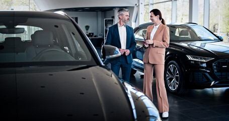 Confident caucasian female trader with tablet opening car door for the customer. Successful businessman choosing new automobile. Car dealership, car business.