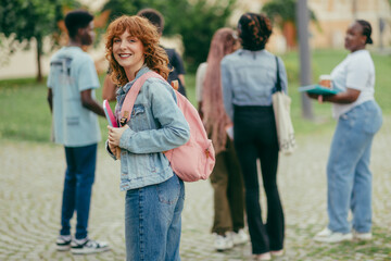 Smiling female university student with backpack and textbook at campus