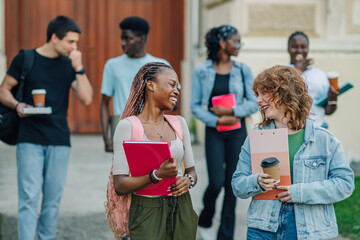 Happy diverse students walking towards camera near university building