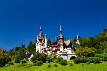 Fototapeta premium The Peles castle in the town of Sinaia, Transylvania, Carpathian Mountains, Romania, Summer time, bright sunny day with dark blue sky. The Peles castle is one of the most beautiful castles in Europe.