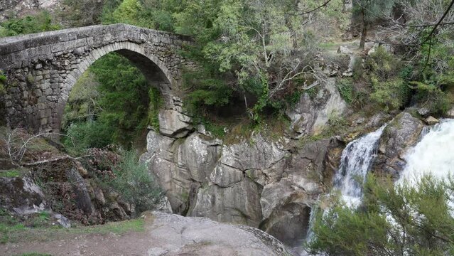 View of the ancient roman Ponte Mizarela, or Devils Bridge with a beautiful arch and picturesque waterfall, at the Peneda Geres National Park in Portugal, Europe