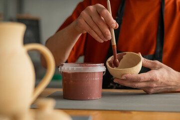 Close-up of a potter's hands with a brush painting ceramic dishes. 