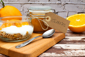 Glass jar full of muesli and yogurt with homemade orange jam, delicious snack with cheesecake and orange jam on wooden cutting board, detail with vintage cardboard tag