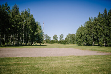Valmiera, Latvia - June 15, 2024 -  A peaceful golf course with green grass, a dirt path, and surrounding trees under a clear blue sky, creating a serene outdoor setting.