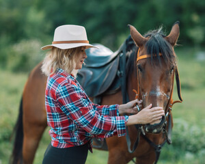 Happy blonde with horse in forest. Woman and a horse walking through the field during the day. Dressed in a plaid shirt and black leggings.