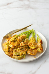 Fried zucchini flowers in batter, plate with zucchini flowers on marble background
