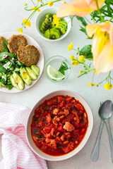 Red soup with beet, beans and vegetables and cauliflower, chickpea cutlets and mixed salad with avocado, delicious hearty breakfasts or lunches, a set table with food and a vase of flowers