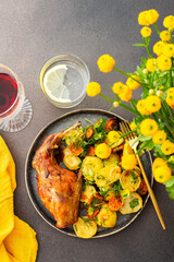 A hearty delicious dinner, baked rabbit with potatoes and carrots, a set table with food, a glass of wine and a vase of flowers