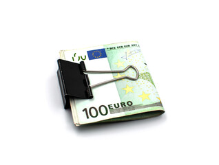 Rolled up hundred euro banknotes clamped with a metal clip on a white background.