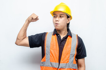 asian construction worker in yellow hard hat and orange vest raising his fist and flexing his bicep to show his power and strenght. strong worker concept.