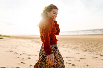 Portrait of cute woman walking along a picturesque sandy beach at sunset in cold weather. Travel,...