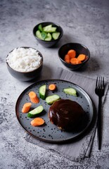 Asian meet hamburger with sauce, rice and vegetables in a plate